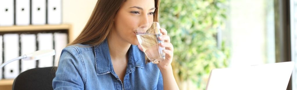 mujer bebiendo un vaso de agua en su escritorio